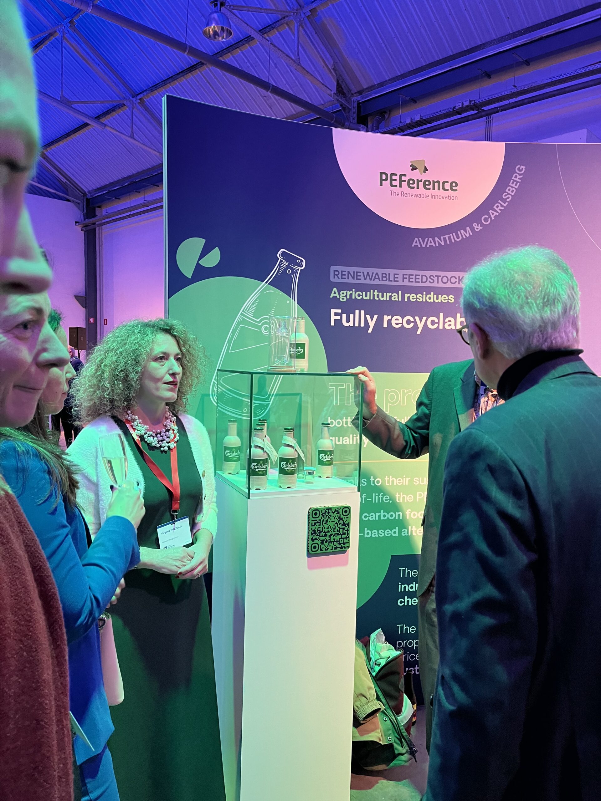 Virginia Puzzolo opens the Carlsberg Group's paper bottles in a glass display to an interested audience. Green and violet lights.