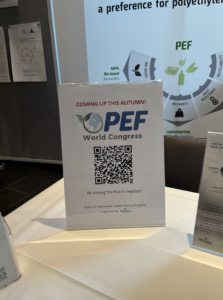 Detail of the PEFerence booth only showing a clipping from the table with the stand-up display informing on the PEF World Congress.In the background is a part of the PEFerence roll-up banner.